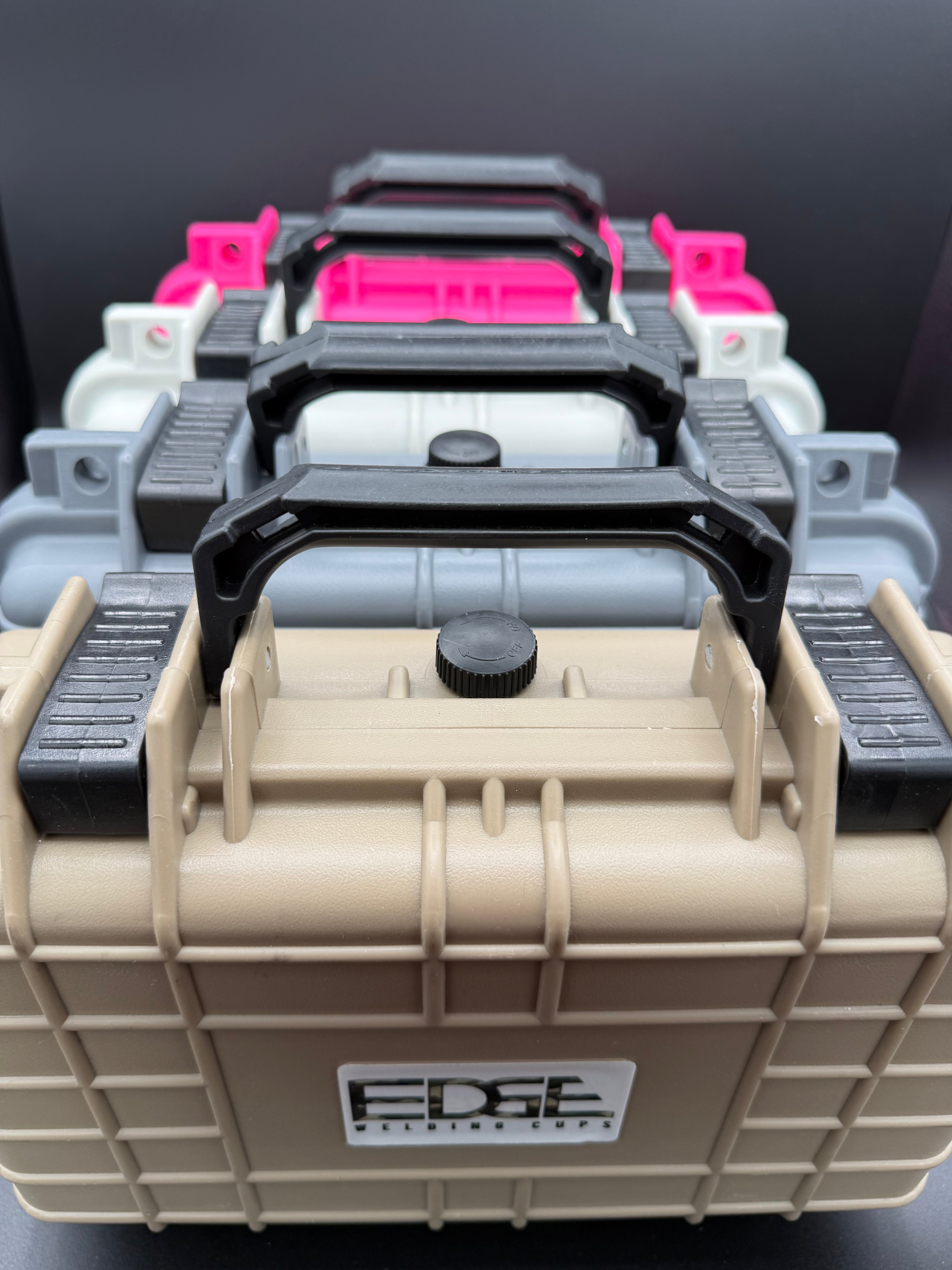 Stack of durable plastic welding equipment storage cases in tan, gray, white, and pink