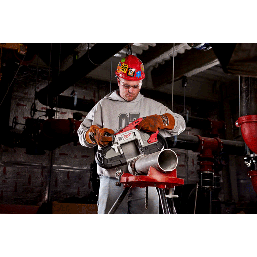 Worker with red hard hat using portable band saw to cut metal pipe in industrial setting